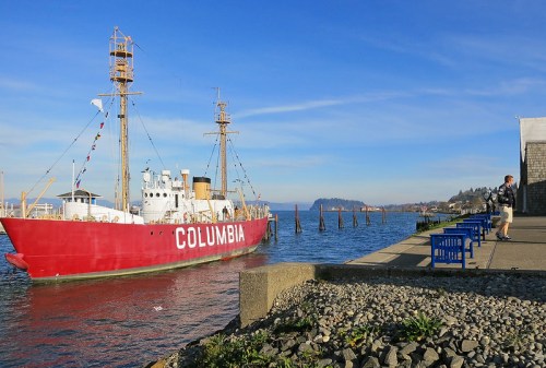 A red ship named "Columbia" docked by a waterfront, with a person sitting on a blue bench nearby.