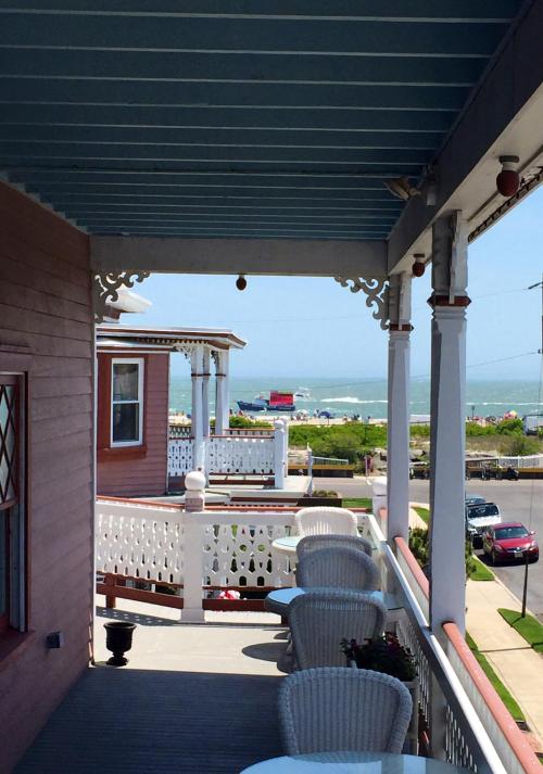 View from a porch with white chairs, overlooking a beach and ocean in the distance on a sunny day.