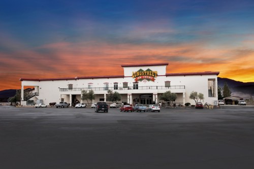 A large casino building at sunset, with parked cars and mountains in the background.