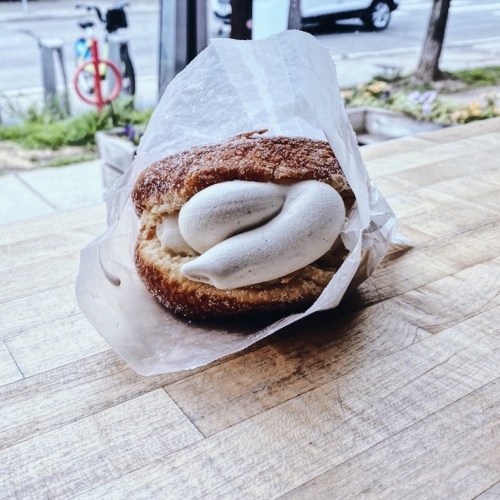 A pastry wrapped in paper, featuring a fluffy donut filled with creamy white filling, resting on a wooden table.