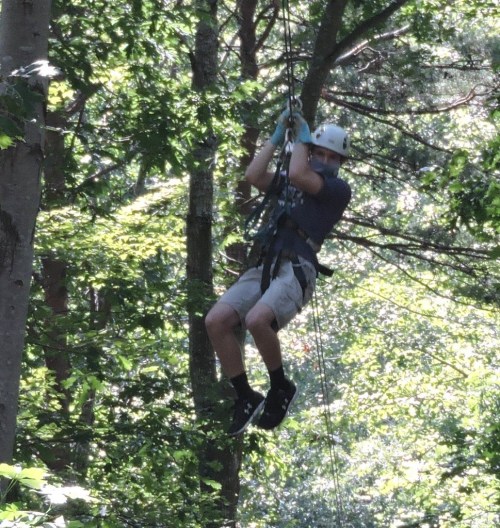 A person in a helmet zip-lining through a forest, surrounded by lush green trees.