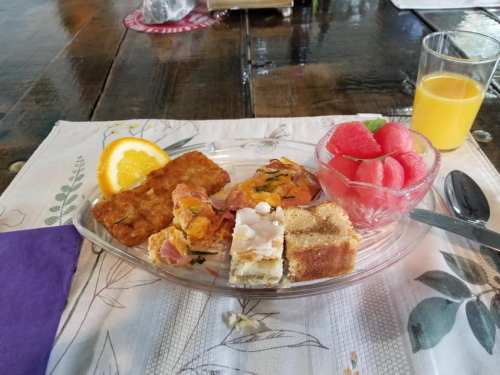 A plate with a variety of pastries, fruit, and a glass of orange juice on a table with a floral tablecloth.