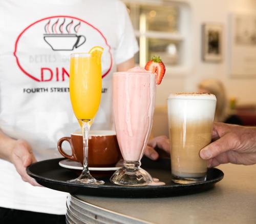 A tray with three drinks: a mimosa, a strawberry milkshake, and a latte, served in a diner setting.