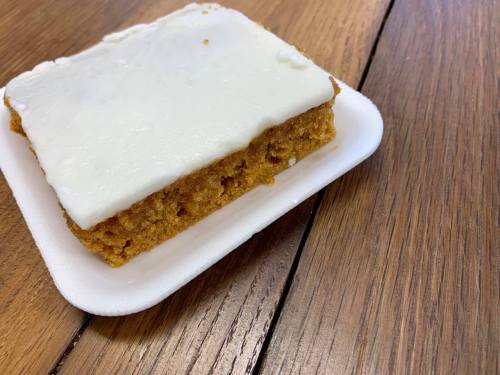 A square piece of cake with white icing on a foam plate, resting on a wooden table.
