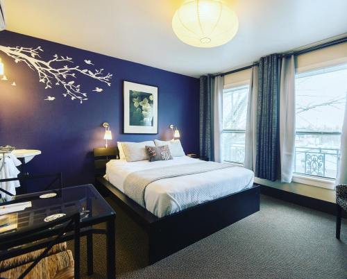 Cozy bedroom with a purple accent wall, a queen bed, and large windows, featuring modern decor and a small table.