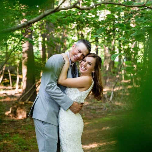 A happy couple embraces in a forest, smiling joyfully, surrounded by greenery on their wedding day.