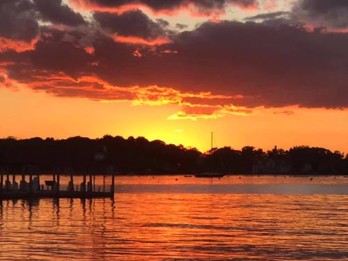 Sunset over a calm lake, with vibrant orange and purple clouds reflecting on the water and silhouettes of trees in the background.