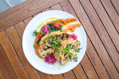 A plate of roasted cauliflower with colorful sauces and garnishes, served on a wooden table.
