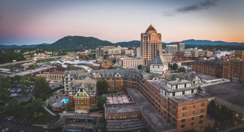 Aerial view of a city skyline at sunset, featuring modern buildings and mountains in the background.
