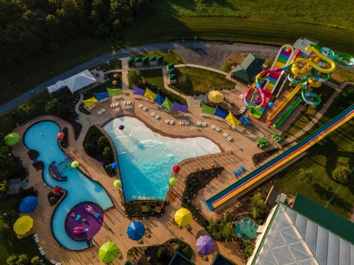 Aerial view of a vibrant water park featuring pools, colorful slides, and umbrellas in a lush green setting.