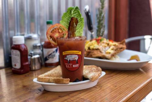 A Bloody Mary garnished with lettuce, tomato, and bacon, served with toast on a wooden table.