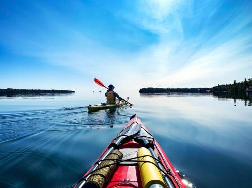 A kayaker paddles on a calm lake, with clear blue skies and reflections on the water.