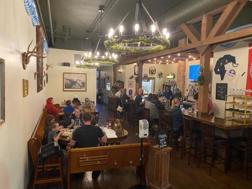 A cozy restaurant interior with diners at tables and a bar, featuring rustic decor and warm lighting.