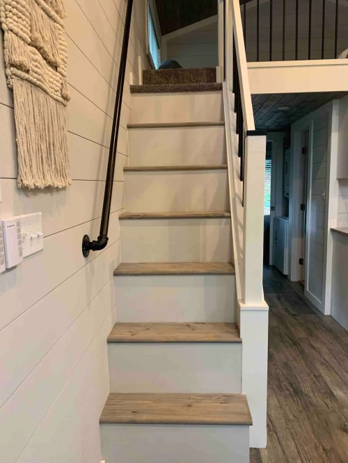 A set of wooden stairs leading to a loft, with a black railing and light-colored walls.