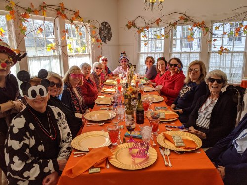 A group of cheerful women wearing fun hats and glasses, gathered around a festive table decorated for a celebration.