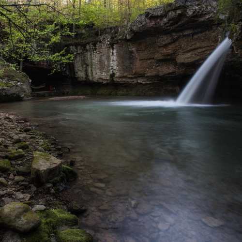 A serene waterfall cascades into a tranquil pool, surrounded by lush greenery and rocky cliffs.