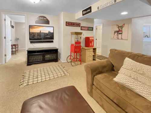 Cozy basement living area with a TV, sofa, popcorn machine, and decorative signs. Warm, inviting atmosphere.