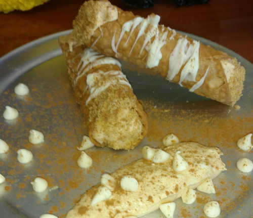 Three cannoli drizzled with icing, sprinkled with cinnamon, on a silver plate with dollops of cream.