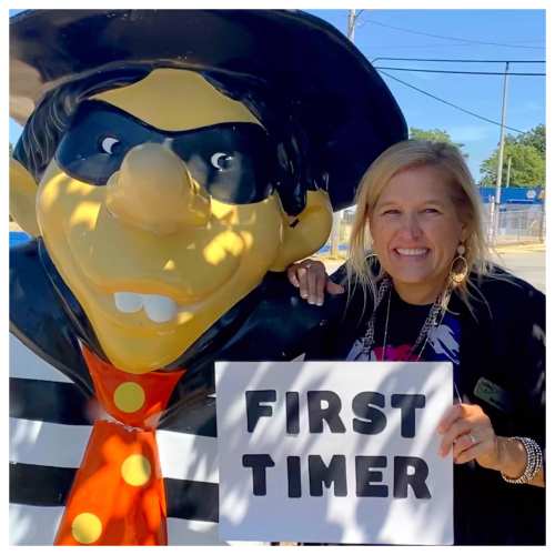A woman poses with a cartoonish pirate statue, holding a sign that says "FIRST TIMER."