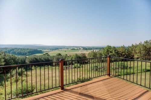 A scenic view from a balcony overlooking lush green fields and distant hills under a clear blue sky.