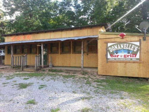 A rustic wooden building with a sign reading "Donanelle's Bar & Grill," surrounded by gravel and trees.