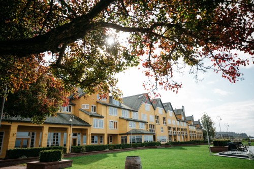 A yellow building with multiple windows, surrounded by green grass and trees with autumn leaves under a bright sky.