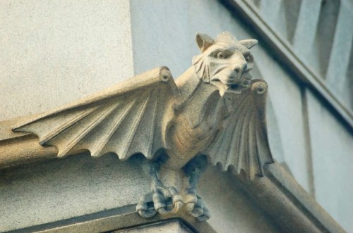 A stone gargoyle with wings and a fierce expression perched on a building corner.