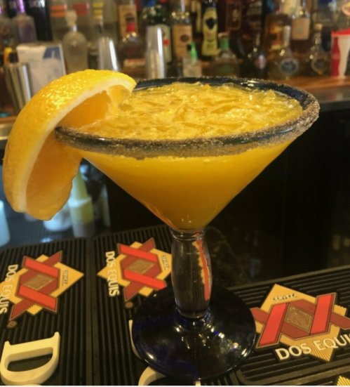 A vibrant margarita with a salted rim, garnished with an orange slice, sits on a bar counter.
