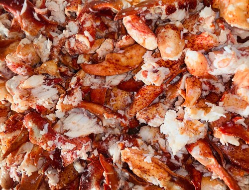 A close-up of a pile of cooked lobster claws and meat, showcasing their red and white textures.