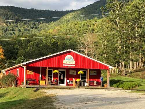 A red barn-style building with a sign, surrounded by green trees and mountains under a partly cloudy sky.