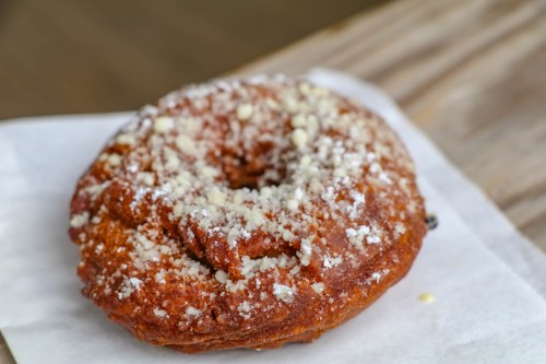 A close-up of a glazed donut topped with powdered sugar, resting on a piece of parchment paper.