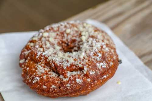 A close-up of a glazed donut topped with powdered sugar, resting on a piece of parchment paper.