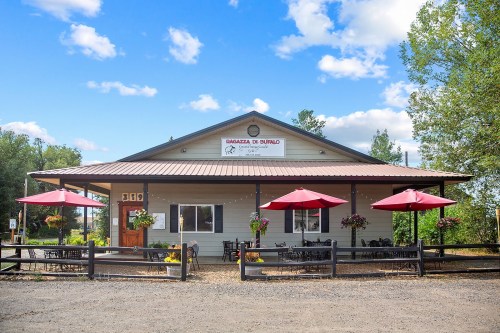 A charming restaurant with a welcoming facade, outdoor seating, and red umbrellas under a blue sky.