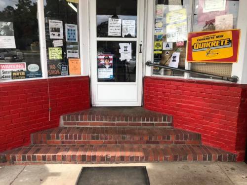 Entrance with red brick steps leading to a door, surrounded by various signs and notices on the windows.