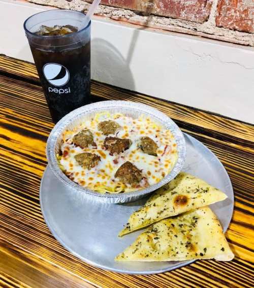 A plate with cheesy pasta and meatballs, accompanied by garlic bread and a cup of Pepsi.