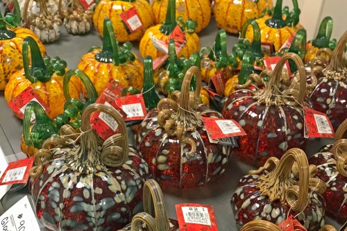 Colorful glass pumpkins in various sizes and designs, displayed on a table with price tags attached.