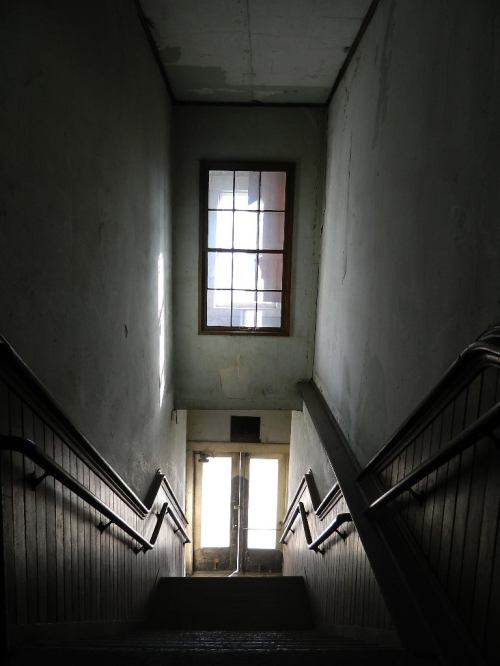 A dimly lit staircase leads down to a door, with a window above casting light into the space.