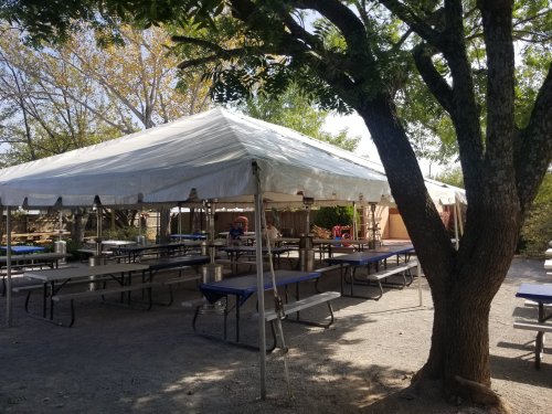 A large white tent with tables and chairs set up underneath, surrounded by trees in an outdoor setting.