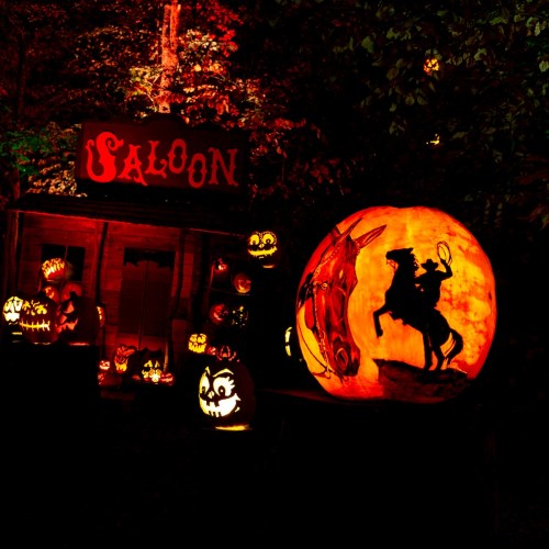 A spooky Halloween scene featuring carved pumpkins, a saloon sign, and a large pumpkin depicting a cowboy on a horse.