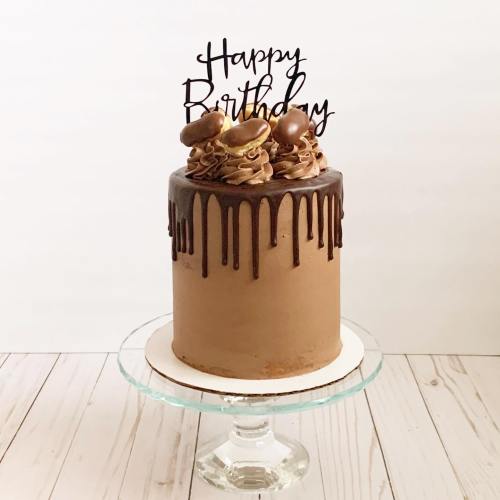 A chocolate birthday cake with a drip effect, topped with cookies and a "Happy Birthday" sign.