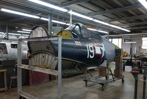 A vintage aircraft fuselage in a workshop, partially restored, with a blue exterior and the number 19 displayed.