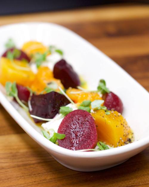 A white dish with colorful beet and orange slices, topped with microgreens and drizzled with dressing.