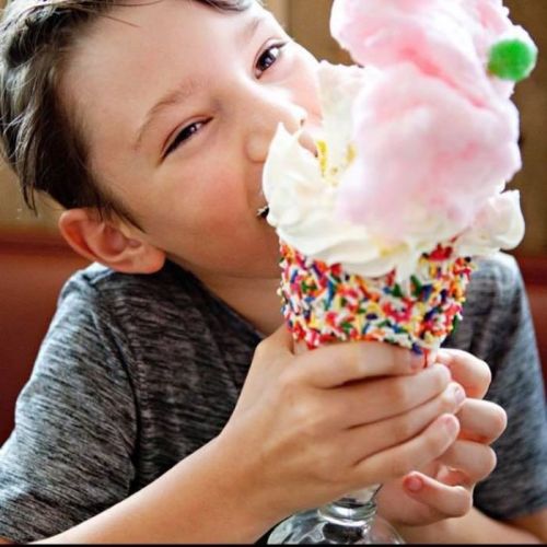 A smiling child enjoys a colorful ice cream sundae topped with whipped cream and cotton candy.