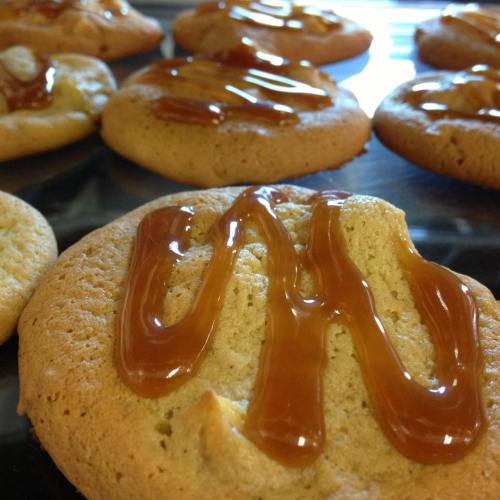 Close-up of freshly baked cookies drizzled with caramel sauce on a baking tray.