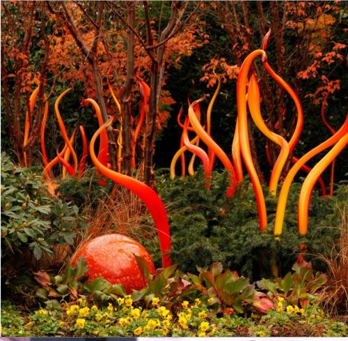Colorful glass sculptures resembling flames amidst vibrant autumn foliage and lush greenery in a garden setting.