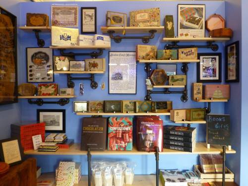 A wall display featuring shelves with various vintage items, books, and framed pictures against a blue background.
