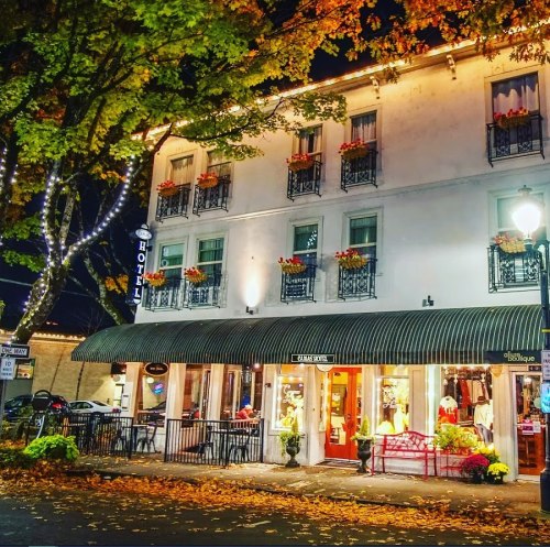 A charming hotel at night, adorned with autumn leaves and warm lights, featuring outdoor seating and flower boxes.