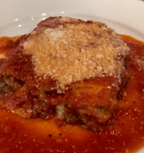 A serving of lasagna topped with marinara sauce and grated cheese on a white plate.