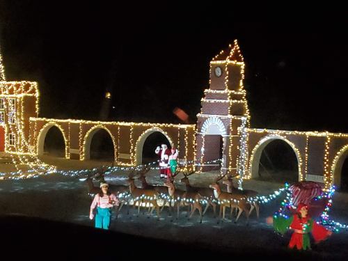 A festive display featuring Santa, reindeer, and colorful lights on a bridge structure at night.