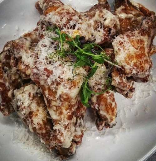 A plate of crispy chicken wings topped with melted cheese and fresh herbs.